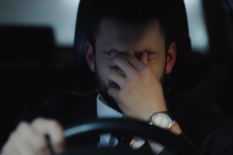sleepy businessman touching eyes while driving car in evening