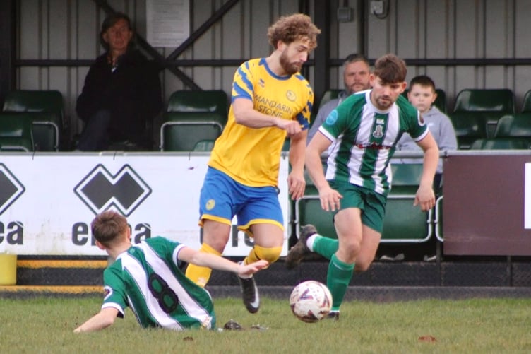 Monmouth Town's Robbie Atkinson drives past two Caerleon defenders