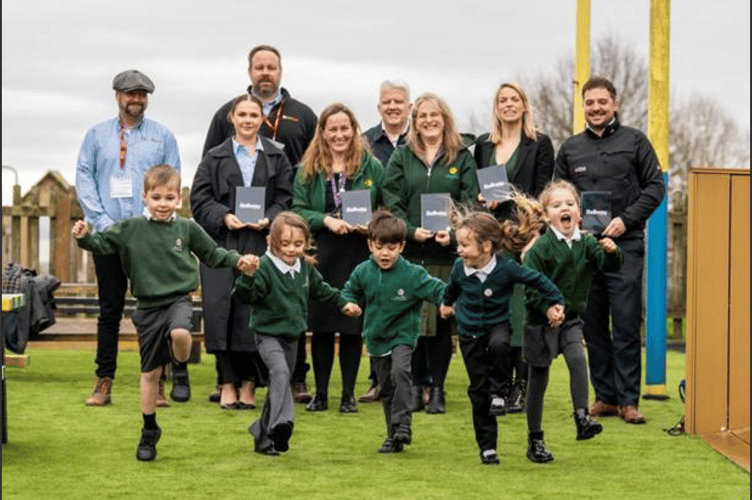 Children from Primrose Hill CofE Primary Academy enjoy using the new play surface, watched by (from left, back) Tom Lord and Oliver Smith from EcoVigour, Simon Hughes from Bellway, Sophie Kelly and Ryan Howell from Miracle Design and Play and (in front) Felicity Milliner from K W Bell and Emma Mignaud and Debbie Mabbutt from the school. 